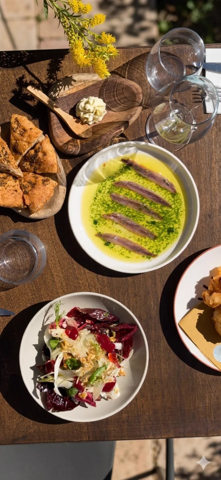 An outdoor table with anchovies, bread and mimosa