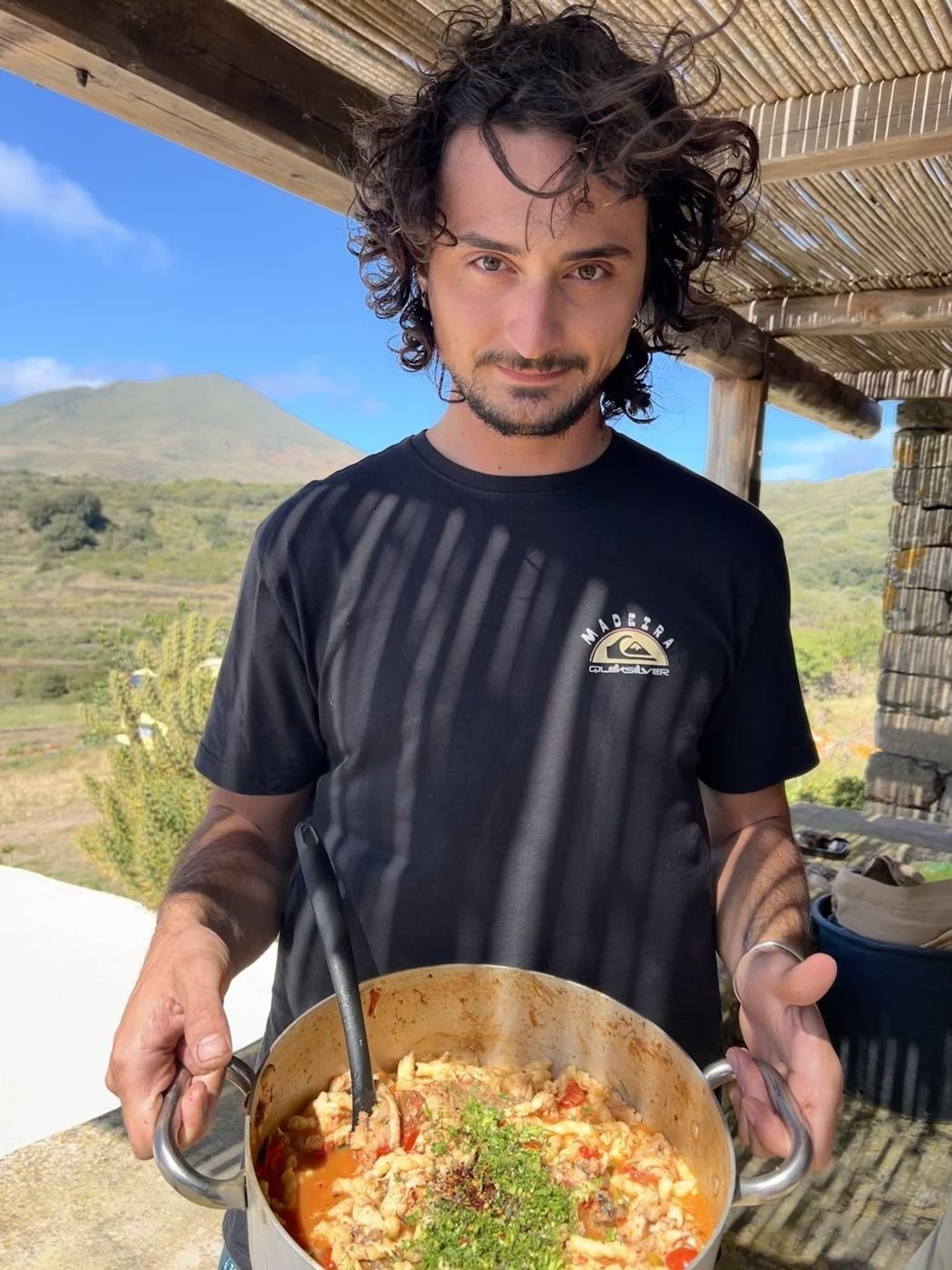 Holding a pan of paella under the pergola